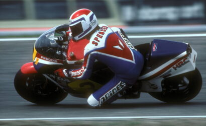 Motorcycle racer in red, white, and blue leathers leaning into a corner on a sportbike during a race.