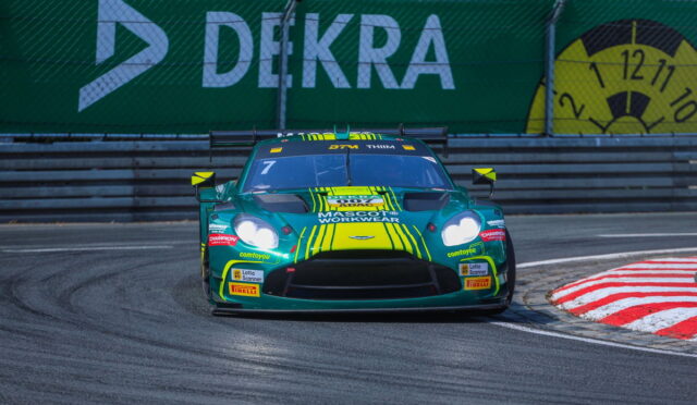 Green race car with bright yellow accents and sponsor logos speeding through a curving race track, barriers and a large Debka banner in the background