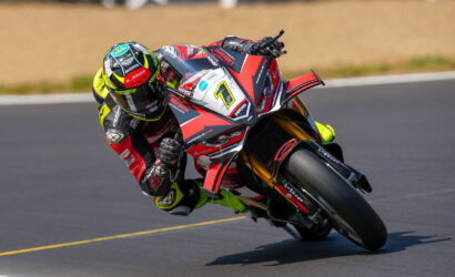 Racing motorcyclist in a yellow-green helmet and red‑white bike leans into a sharp turn on a race track.