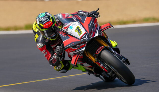 Racing motorcyclist in a yellow-green helmet and red‑white bike leans into a sharp turn on a race track.