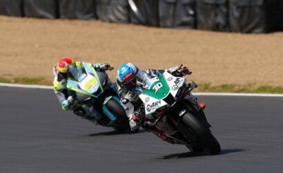 Two motorcycle racers lean into a sharp turn on a race track, bikes close together mid-race.