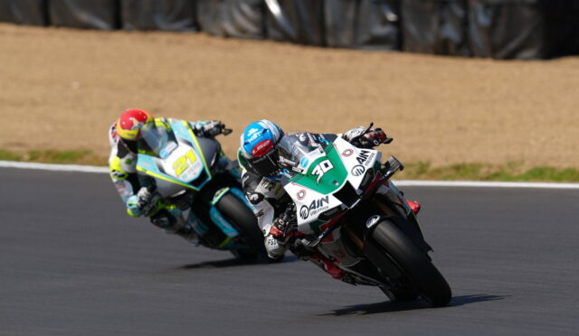 Two motorcycle racers lean into a sharp turn on a race track, bikes close together mid-race.
