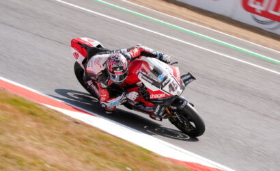 Motorcycle racer in red-and-white gear leaning into a corner on a race track, rider numbered 41 with sponsor logos visible on the bike and suit.