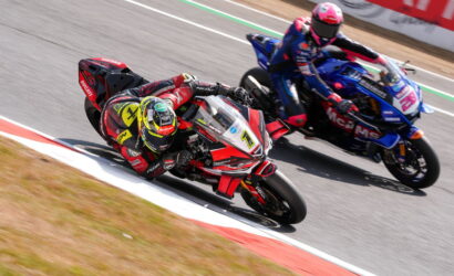 Two motorcycle racers lean into a right-hand corner on a racetrack, red Ducati ahead and blue Yamaha close behind.