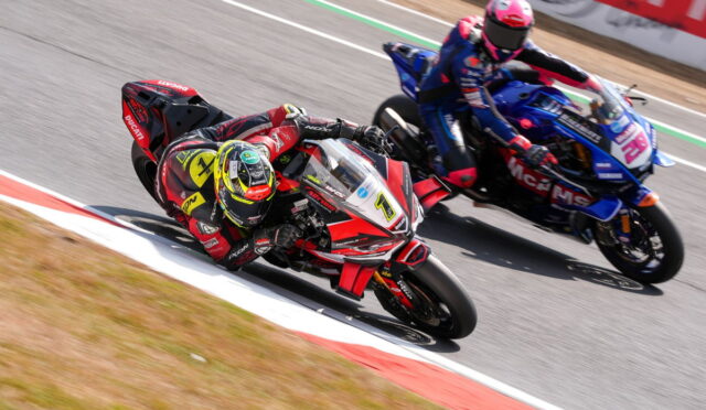 Two motorcycle racers lean into a right-hand corner on a racetrack, red Ducati ahead and blue Yamaha close behind.