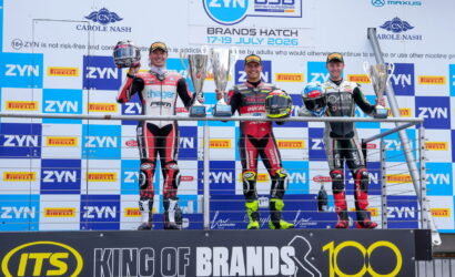 Four motorcycle racers on a winners' podium holding trophies at Brands Hatch, with sponsor banners in the background.