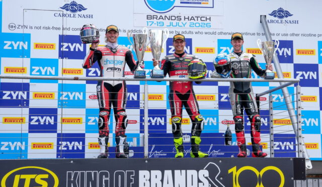 Four motorcycle racers on a winners' podium holding trophies at Brands Hatch, with sponsor banners in the background.