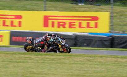 Motorcycle racer leaning into a sharp turn on a race track with prominent Pirelli banners in the background