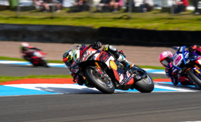 Motorcycle race: rider leaning sharply into a turn on a colorful track, other racers blurred in the background.