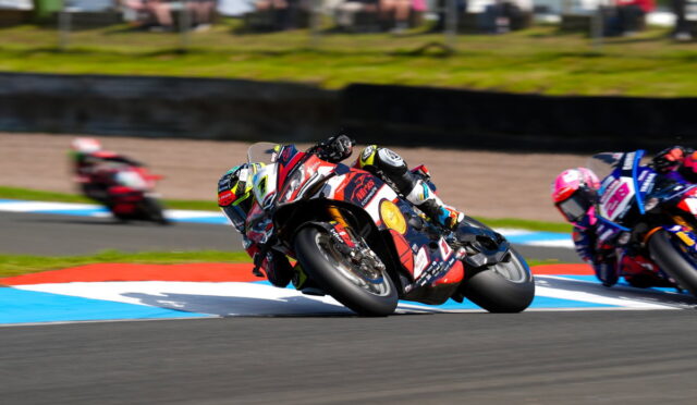 Motorcycle race: rider leaning sharply into a turn on a colorful track, other racers blurred in the background.