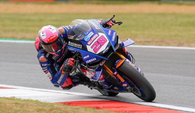 Motorcycle racer in blue and pink gear leaning into a turn on a blue Yamaha race bike with number 28 on the fairing.