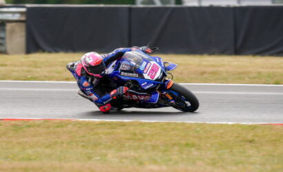 Motorcycle racer in blue and pink gear leans into a left-hand turn on a race track, bike number 28.