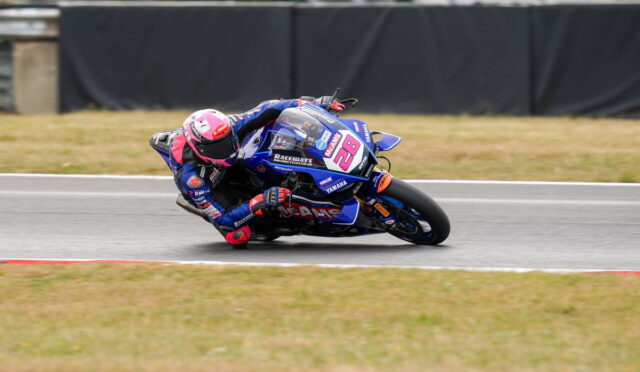 Motorcycle racer in blue and pink gear leans into a left-hand turn on a race track, bike number 28.