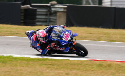 Motorcycle racer in a pink helmet leaning into a curve on a racetrack, blue Yamaha bike number 28.