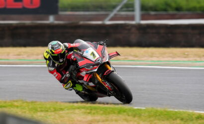 Motorcycle racer leaning into a sharp turn on a race track, red-black suit and bike in focus at speed