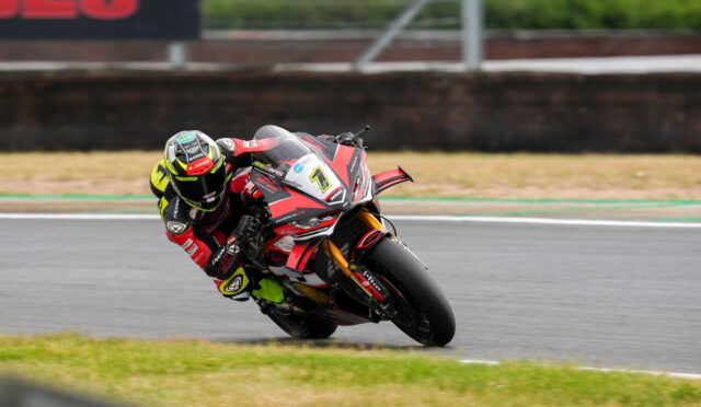 Motorcycle racer leaning into a sharp turn on a race track, red-black suit and bike in focus at speed