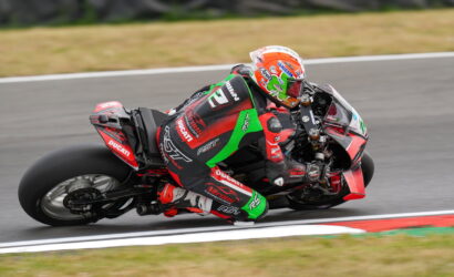 Motorcycle racer in red-green suit leaning into a curve on a race track, Ducati branding visible on bike and suit