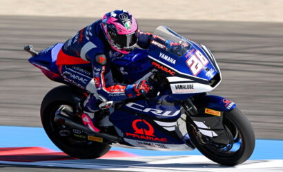 Rider in blue and red racing gear on a blue Yamaha race bike, number 28, leaning into a turn on a racetrack