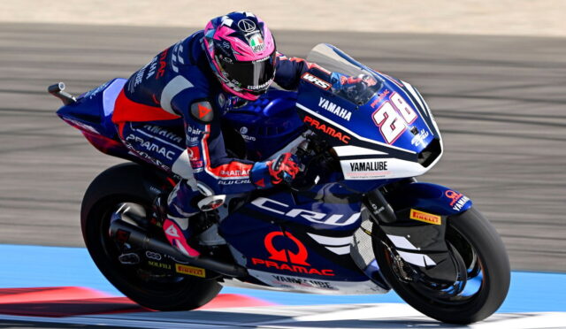 Rider in blue and red racing gear on a blue Yamaha race bike, number 28, leaning into a turn on a racetrack