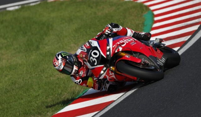 Motorcycle racer in red and white gear leans into a corner on a racetrack, bike number 30.