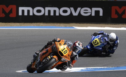 Two motorcycle racers lean into a turn on a race track; orange bike #10 ahead of blue bike #51 in pursuit.