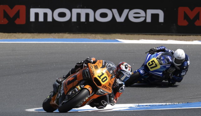Two motorcycle racers lean into a turn on a race track; orange bike #10 ahead of blue bike #51 in pursuit.