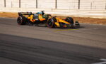 Orange and black Formula 1 car speeding along a race track with guard rails in the background.
