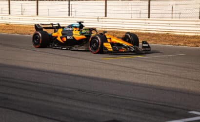 Orange and black Formula 1 car speeding along a race track with guard rails in the background.