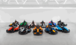 Assortment of colorful go-karts arranged in neat rows on a gray concrete floor in an indoor space.