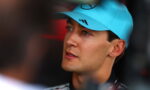 Close-up of a man wearing a bright blue cap with a Mercedes logo, looking off to the left in a thoughtful gaze.