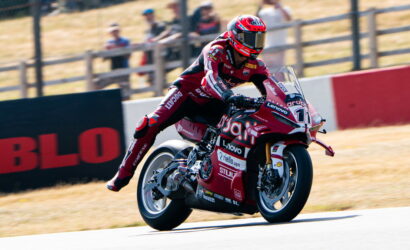 Motorcycle racer in red racing suit speeding on a track, leaning into a turn on a red sponsorship bike with number 11