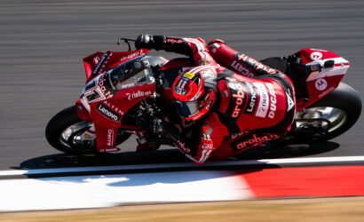 Two MotoGP riders in red Aruba.it Ducati livery lean into a sharp corner on a race track, close together at speed.