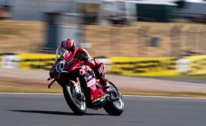 Motorcycle racer in a red racing suit leans into a curve on a race track with motion blur in the background.