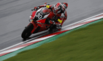 Rider on a red Honda motorcycle leaning into a sharp turn on a race track, number 30 visible on the bike's front plate.