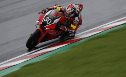 Rider on a red Honda motorcycle leaning into a sharp turn on a race track, number 30 visible on the bike's front plate.