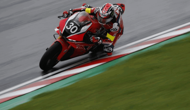 Rider on a red Honda motorcycle leaning into a sharp turn on a race track, number 30 visible on the bike's front plate.