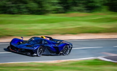 Blue high-performance race car speeding along a curved racetrack with green grass and blur in the background.