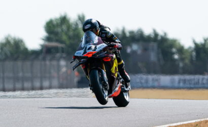 Motorcycle racer wearing a black helmet and yellow‑black gear leans into a turn on a racetrack at speed