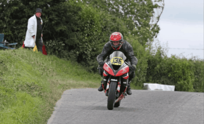 Motorcycle racer in a red helmet and black gear leaning into a curve on a rural road, bike #136.