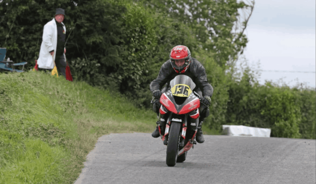 Motorcycle racer in a red helmet and black gear leaning into a curve on a rural road, bike #136.
