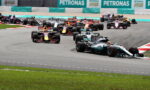 Multiple Formula 1 cars racing on a track, turning, with Petronas banners in the background. (Informative)