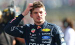 Racing driver in a dark blue Oracle suit runs his hand through his hair, standing outdoors with sponsor logos visible on his suit
