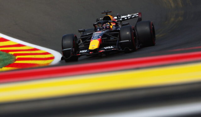 Red Bull Racing Formula 1 car cornering on a race track, visible sponsor logos and red-yellow curbs in the foreground.