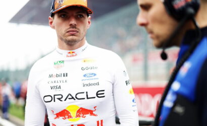 Formula 1 driver in an Oracle Red Bull Racing suit and orange cap on the pit lane, looking toward the camera.