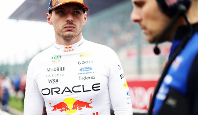 Formula 1 driver in an Oracle Red Bull Racing suit and orange cap on the pit lane, looking toward the camera.