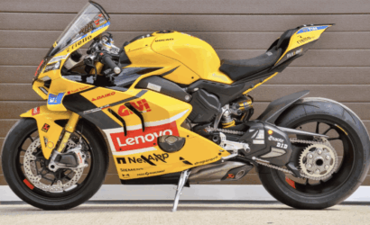 Yellow MotoGP racing motorcycle with Lenovo sponsorship logos, parked on a kickstand on a wooden backdrop.