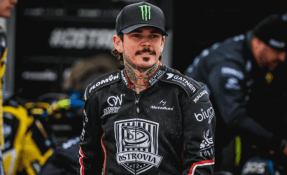 Motocross rider wearing a black Ostrovia racing jersey and a Monster cap in the pit area.
