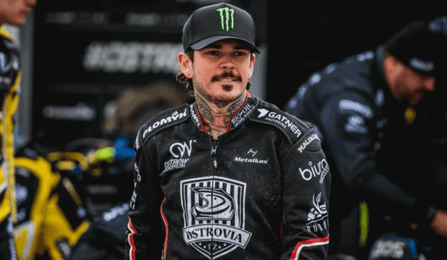 Motocross rider wearing a black Ostrovia racing jersey and a Monster cap in the pit area.