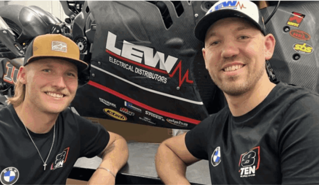 Two smiling men in black T-shirts sit beside a black race car with LEW Electrical Distributors branding in the background.
