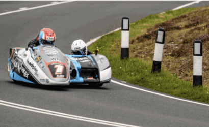Sidecar motorcycle race rounding a bend on a paved road with white lane markings.